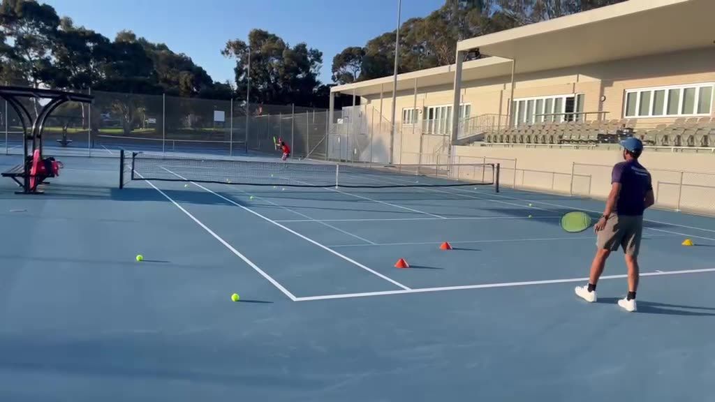 A coach feeding balls across the net during a squad session
