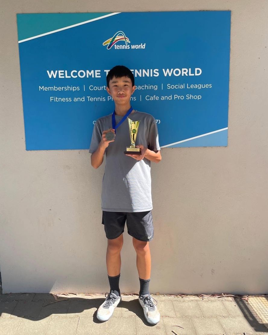A junior player holding a trophy at a tournament venue