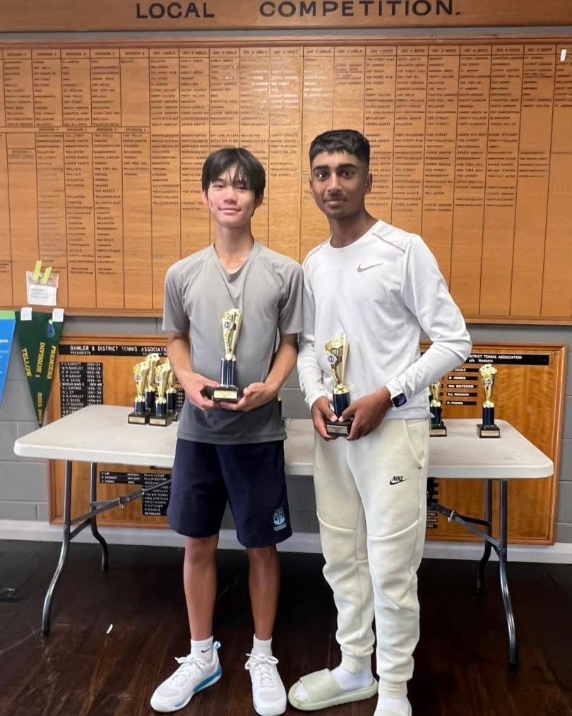 Two junior players with trophies in front of a club honour board
