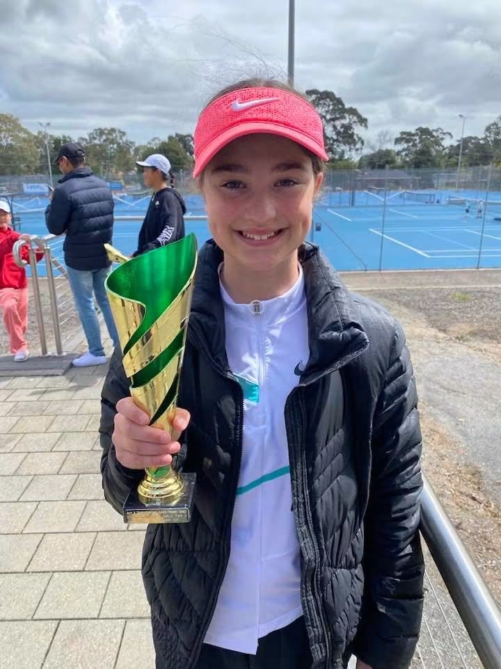 A junior player holding a trophy at a tournament venue