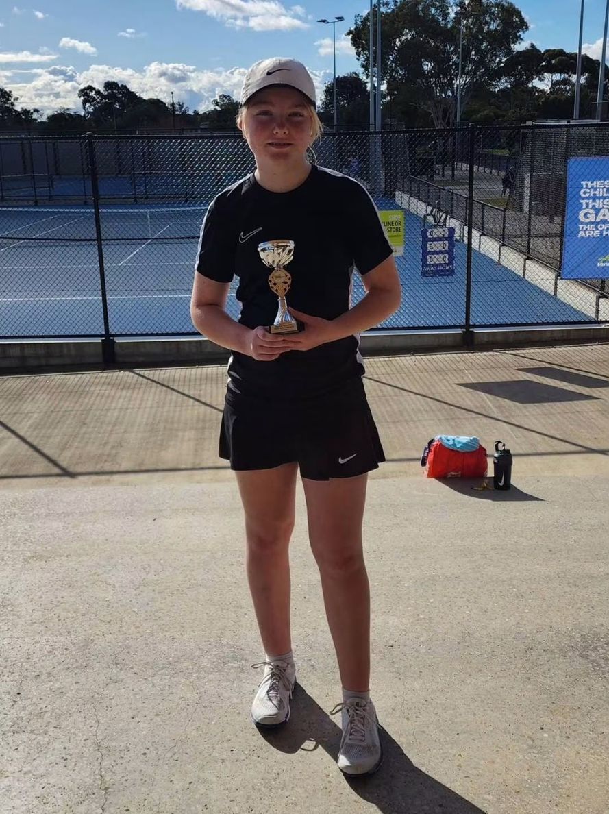 A junior player holding a trophy courtside