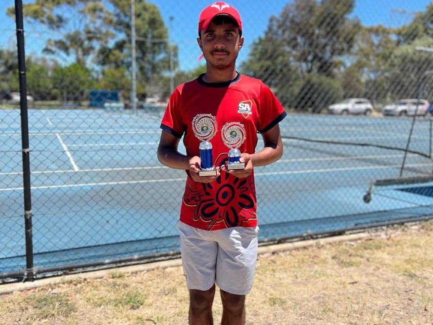A junior player holding a trophy courtside