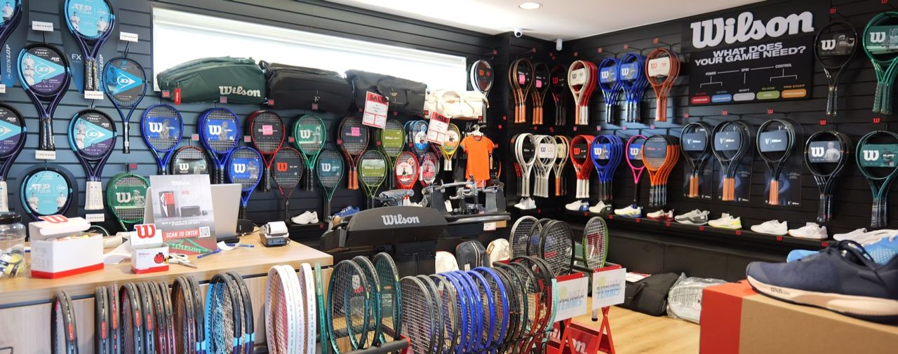 The Just 4 Tennis pro shop floor, racquets and shoes on the walls and a stringing machine on the counter