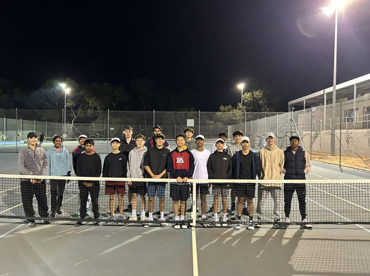 A camp group at the net on the floodlit courts after an evening session