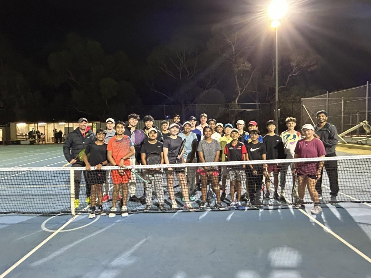 A camp group with racquets gathered behind the net at night