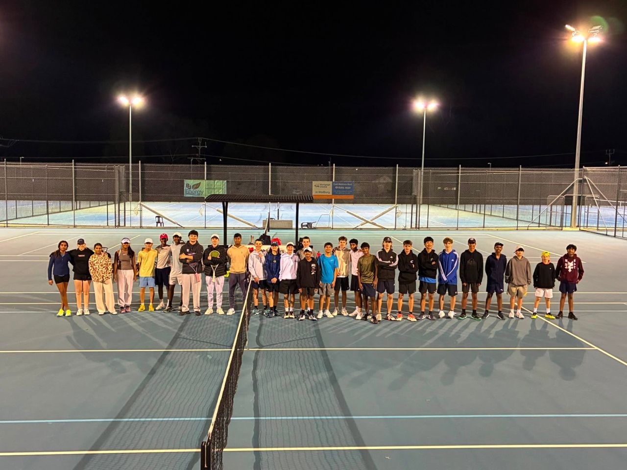 A camp group spread along the baseline across two floodlit courts
