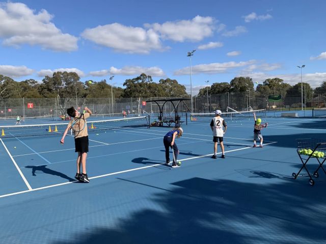 A junior group session in progress on the outdoor courts on a clear day