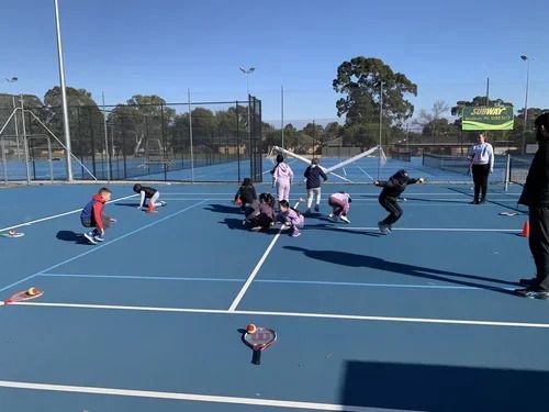 A group of juniors gathered mid-court during a session, with racquets and balls on the ground around them